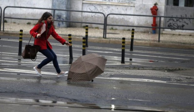 A woman tries to catch her umbrella after it was blown away by the wind in downtown Lisbon