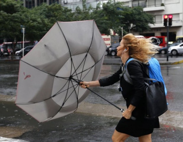 A woman struggles to control her umbrella from the wind during rainfall in Buenos Aires