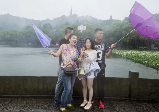 Tourists hold umbrellas as they take a picture with a selfie stick next to the West Lake against strong wind under the influence of Typhoon Chan-hom, in Hangzhou