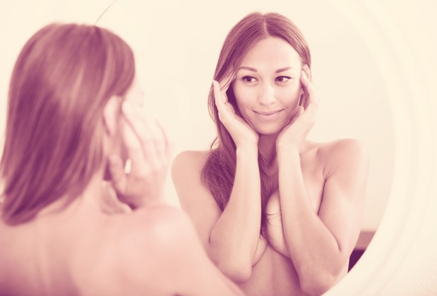 naked woman attentively looking at herself in mirror